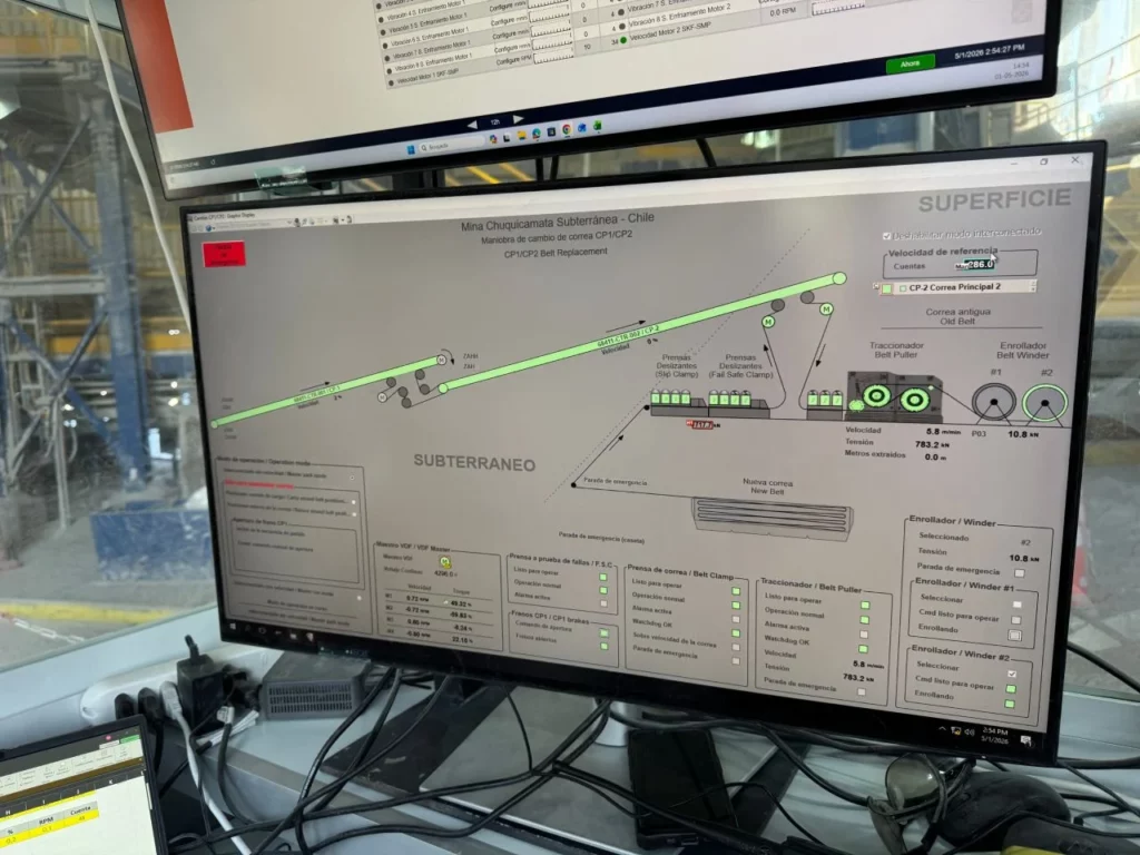 A computer monitor displays a detailed schematic diagram of a subterranean mine in Chile, labelled "Subterráneo" and "Superficie," with various indicators, green lines, and control panels. Cables and other screens are visible nearby.